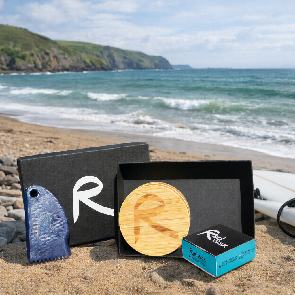 Rad Wax Gift Set. A Surfboard Wax Gift Set.Wooden product with 'R' logo on a beach with ocean and cliffs in the background