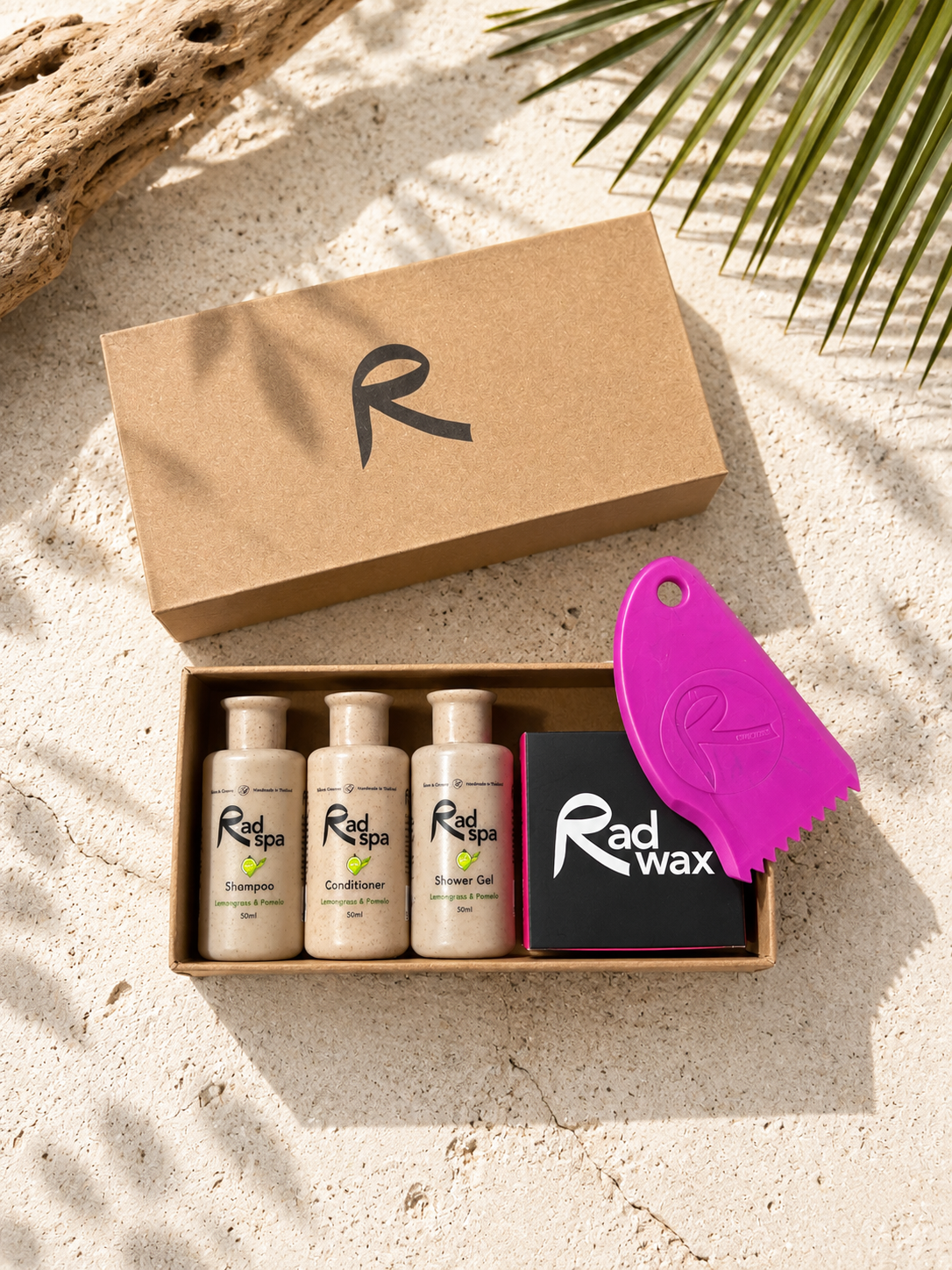 Rad Wax hair care product set with bottles and a purple tool on sand