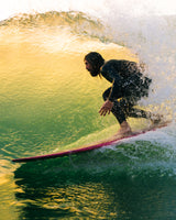Person surfing on a wave with a colorful surfboard. Rad Wax Surfer High Performance Eco Wax