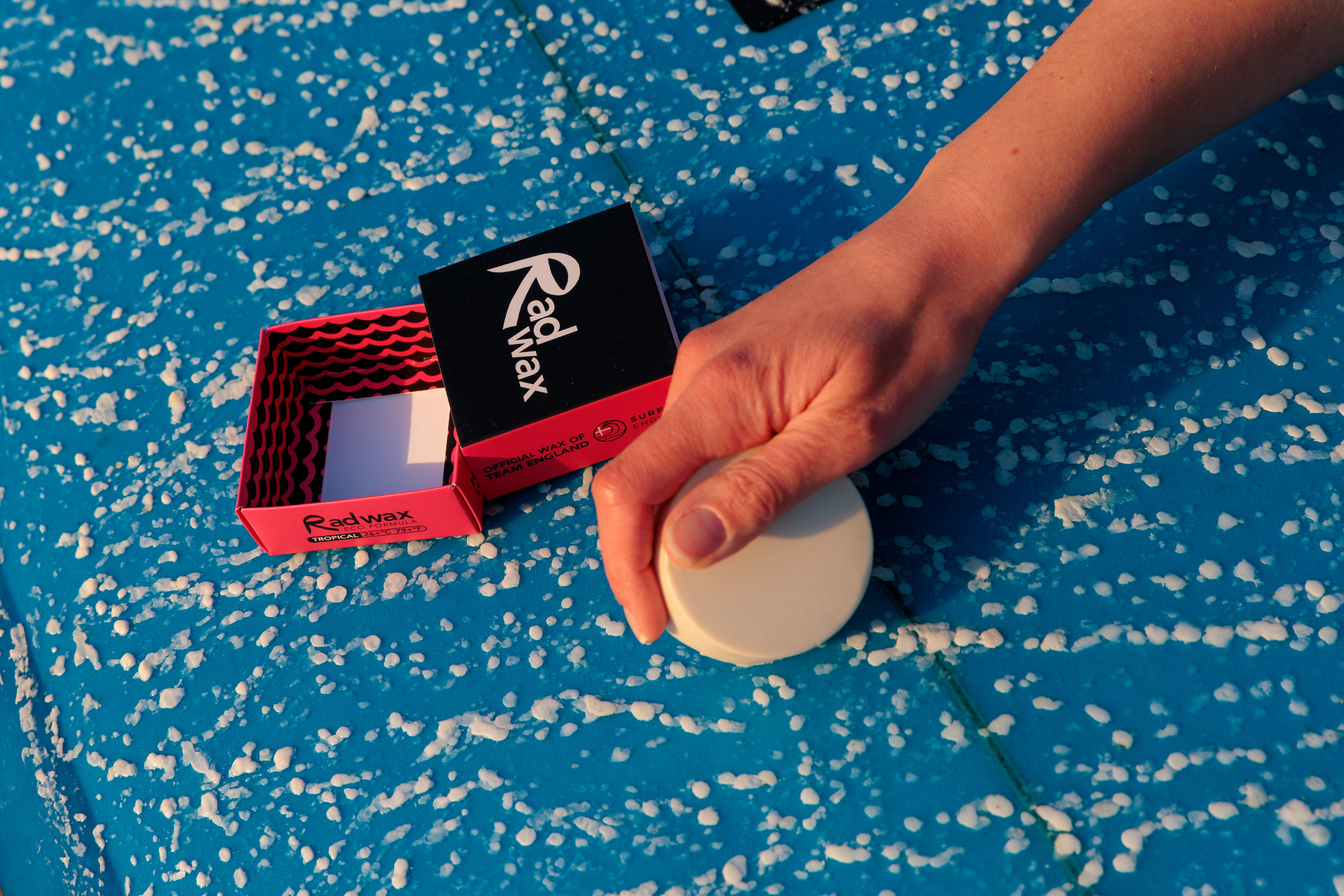 Surfer waxing a board with Rad Wax Tropical Top Coat