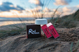 Rad Wax Tropical Eco Surf Wax on a sandy beach with grass and water in the background